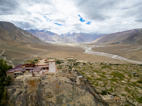 Aerial view of Karsha Monastery perched on a rocky cliff overlooking the Zanskar River valley with terraced fields and snow capped Himalayan peaks in Zanskar Ladakh India.