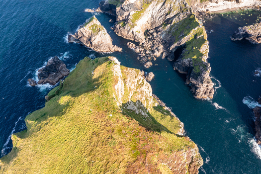 Aerial view of the rugged cliffs and green grassy slopes of Glenlough Bay meeting the deep blue Atlantic Ocean in Ardara County Donegal Ireland.