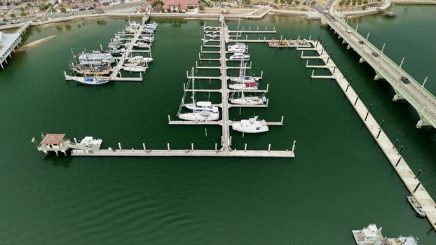 Aerial view of boats docked at a marina next to a bridge and urban shoreline with green water in St. Augustine Florida United States.