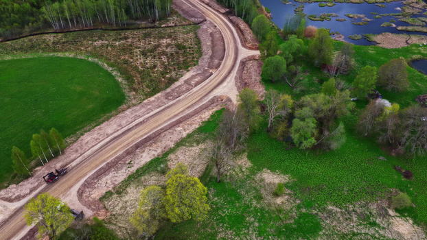 Aerial view of a dirt wind turbine maintenance road winding through green fields and lush trees in Latvia. Aerial view of a dirt wind turbine maintenance road winding through green fields and lush trees in Latvia.