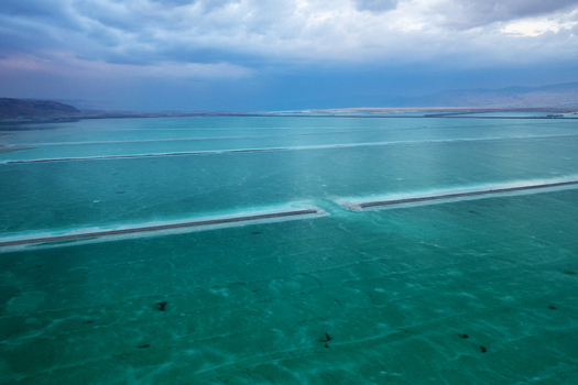 Aerial view of the mesmerizing turquoise waters of the Dead Sea shimmer under a moody sky contrasting with the stark mineral rich shores Arad South District Israel. Aerial view of the mesmerizing turquoise waters of the Dead Sea shimmer under a moody sky contrasting with the stark mineral rich shores Arad South District Israel.