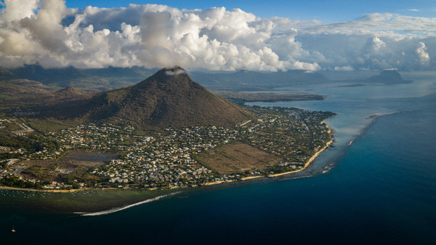 Aerial view of a coastal settlement at the base of a majestic mountain peak under a cloudy sky with turquoise ocean waters Mauritius Moka District Mauritius. Aerial view of a coastal settlement at the base of a majestic mountain peak under a cloudy sky with turquoise ocean waters Mauritius Moka District Mauritius.
