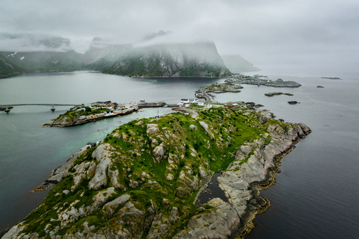Aerial view of Reine in the Lofoten archipelago featuring rocky islands bridges connecting settlements and dramatic mountains under a moody sky in Reine Nordland Norway. Aerial view of Reine in the Lofoten archipelago featuring rocky islands bridges connecting settlements and dramatic mountains under a moody sky in Reine Nordland Norway.