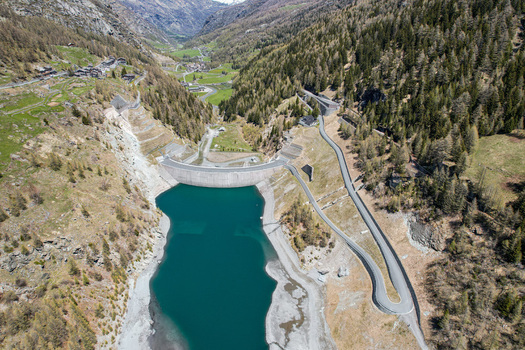 Aerial view of the Beauregard Dam and its turquoise reservoir surrounded by steep alpine slopes and winding roads in Valgrisenche Aosta Valley Italy.