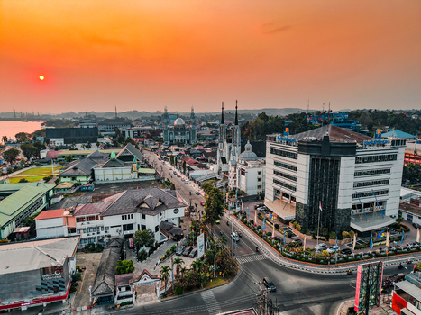 Aerial view of the city skyline at sunset featuring a prominent mosque with a silver dome modern office buildings and busy streets in Samarinda East Kalimantan Indonesia. Aerial view of the city skyline at sunset featuring a prominent mosque with a silver dome modern office buildings and busy streets in Samarinda East Kalimantan Indonesia.