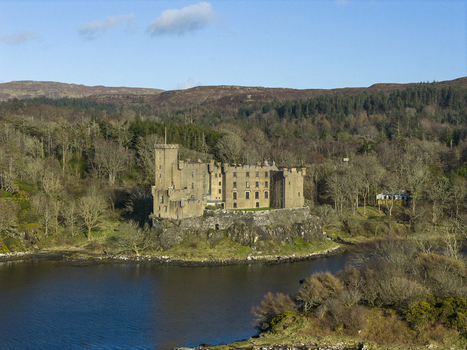 Aerial view of Dunvegan Castle and Gardens situated on a rocky outcrop overlooking the water and surrounded by lush forests and rolling hills in Isle of Skye Scotland United Kingdom. Aerial view of Dunvegan Castle and Gardens situated on a rocky outcrop overlooking the water and surrounded by lush forests and rolling hills in Isle of Skye Scotland United Kingdom.
