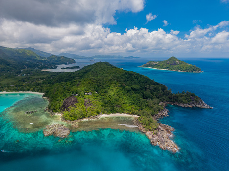 Aerial view of lush green hills cascade into the turquoise sea with rugged rocks meeting the soft sand creating a vibrant contrast of colors Victoria Mahe Island Seychelles. Aerial view of lush green hills cascade into the turquoise sea with rugged rocks meeting the soft sand creating a vibrant contrast of colors Victoria Mahe Island Seychelles.