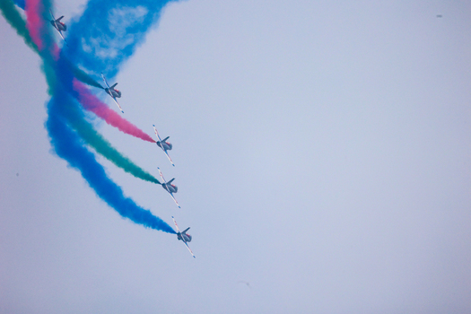 Dhaka Bangladesh 25 March 2026 View of fighter jets soaring through the sky leaving trails of vivid blue green and red smoke against the pale canvas.