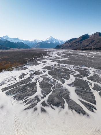 Aerial view of glacial rivers carving intricate paths through the rugged landscape with snow capped mountains piercing the clear sky Lake Tekapo Canterbury Region New Zealand. Aerial view of glacial rivers carving intricate paths through the rugged landscape with snow capped mountains piercing the clear sky Lake Tekapo Canterbury Region New Zealand.