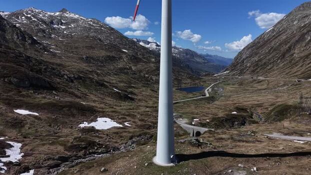 Aerial view of a wind turbine at San Gottardo Wind Park with rocky mountains and snow patches in Airolo Ticino Switzerland.