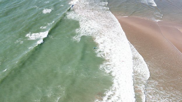 Aerial view of waves crashing on the sandy shoreline of Bantham Beach with a surfer in the turquoise water Kingsbridge Devon United Kingdom. Aerial view of waves crashing on the sandy shoreline of Bantham Beach with a surfer in the turquoise water Kingsbridge Devon United Kingdom.