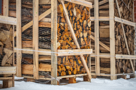 View of stacked firewood in wooden crates wrapped in plastic netting on a snowy ground in Latvia. View of stacked firewood in wooden crates wrapped in plastic netting on a snowy ground in Latvia.