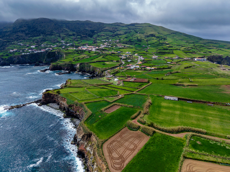 Aerial view of the rugged coastline where the dark blue ocean meets verdant fields and quaint villages nestled amidst the rolling hills Flores A&ccedil;ores Portugal.