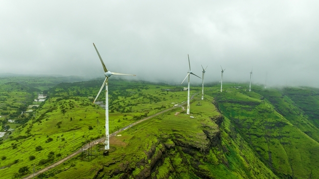 Aerial view of wind turbines standing on a lush green hillside under a misty sky in Igatpuri Maharashtra India. Aerial view of wind turbines standing on a lush green hillside under a misty sky in Igatpuri Maharashtra India.