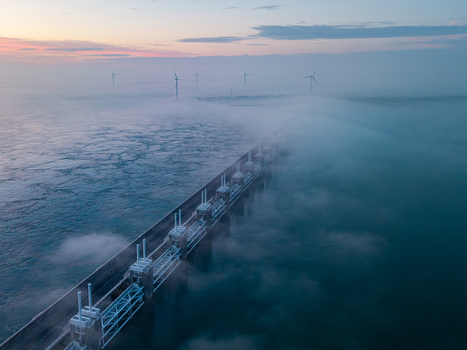 Aerial view of the Delta Projects Netherlands storm surge barrier shrouded in thick morning fog with wind turbines in the distance Vrouwenpolder Zeeland Netherlands.