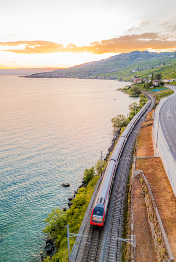 Aerial view of a train traveling along the shore of Lake Geneva through the terraced vineyards of the Lavaux region at sunset in Bourg en Lavaux Vaud Switzerland. Aerial view of a train traveling along the shore of Lake Geneva through the terraced vineyards of the Lavaux region at sunset in Bourg en Lavaux Vaud Switzerland.