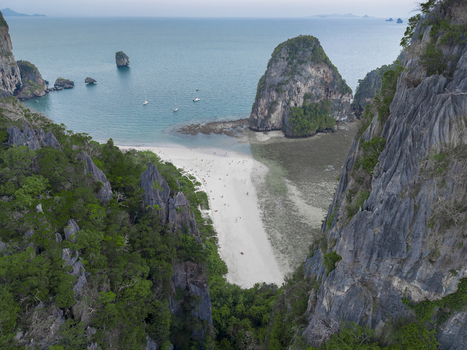 Aerial view of the sandy beach nestled between towering limestone cliffs meeting the turquoise sea Krabi Thailand.