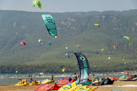 View of kitesurfers with colorful kites on the beach with mountains in the background in Akyaka Mugla Turkey. View of kitesurfers with colorful kites on the beach with mountains in the background in Akyaka Mugla Turkey.