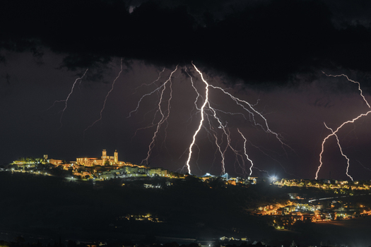 View of multiple lightning bolts striking the night sky over the illuminated historic town of Montecosaro Marche Italy. View of multiple lightning bolts striking the night sky over the illuminated historic town of Montecosaro Marche Italy.