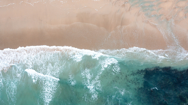 Aerial view of turquoise ocean waves crashing onto the sandy shore of Constantine Bay in Padstow Cornwall United Kingdom. Aerial view of turquoise ocean waves crashing onto the sandy shore of Constantine Bay in Padstow Cornwall United Kingdom.
