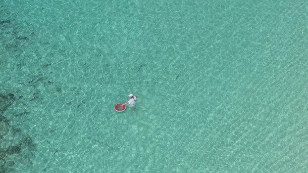 Aerial view of a woman with a swim ring in clear water Maldives.
