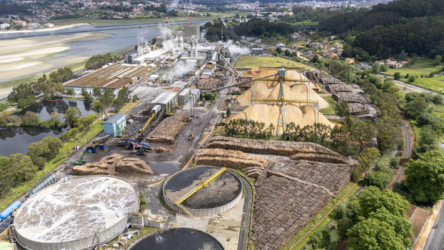 Aerial view of the Biofabrica de Ence industrial complex featuring large wood chip piles steam rising from stacks and circular treatment tanks in Pontevedra Pontevedra Spain. Aerial view of the Biofabrica de Ence industrial complex featuring large wood chip piles steam rising from stacks and circular treatment tanks in Pontevedra Pontevedra Spain.