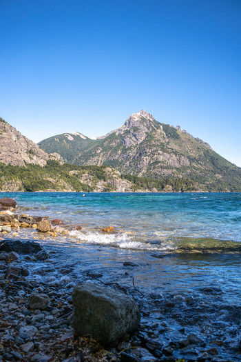 View of the rocky shoreline and turquoise waters of Nahuel Huapi Lake with the majestic Andes mountains in the background in San Carlos de Bariloche Rio Negro Argentina.