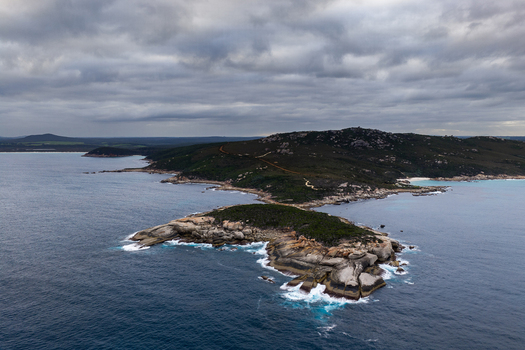 Aerial view of Bettys Beach featuring rugged rocky outcrops crashing waves and lush coastal vegetation under a dramatic cloudy sky in Albany WA Australia. Aerial view of Bettys Beach featuring rugged rocky outcrops crashing waves and lush coastal vegetation under a dramatic cloudy sky in Albany WA Australia.