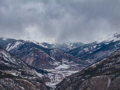 View of snow covered mountain peaks and a valley under a dramatic overcast sky with evergreen forests in Colorado United States.