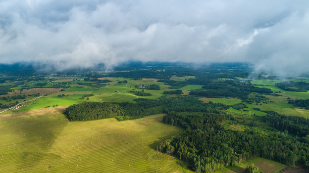 Aerial view of lush green fields and dense forests under a dramatic cloudy sky in the countryside of Latvia. Aerial view of lush green fields and dense forests under a dramatic cloudy sky in the countryside of Latvia.
