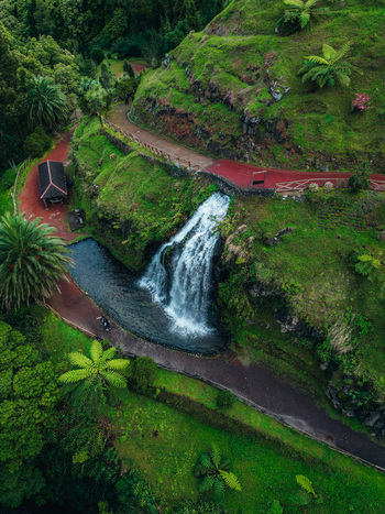 Aerial view of a cascading waterfall plunges into a serene pool surrounded by vibrant green foliage and winding red paths Achada Açores Portugal. Aerial view of a cascading waterfall plunges into a serene pool surrounded by vibrant green foliage and winding red paths Achada Açores Portugal.