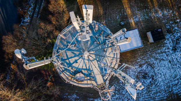 Valmiera Latvia 11 November 2025 Aerial view of a telecommunications tower featuring multiple antennas and satellite dishes surrounded by sparse winter vegetation and patches of snow.