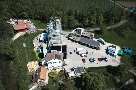 Aerial view of the Moulin de la Vaux industrial complex with tall silver silos and administrative buildings surrounded by lush green forests in Aubonne Vaud Switzerland. Aerial view of the Moulin de la Vaux industrial complex with tall silver silos and administrative buildings surrounded by lush green forests in Aubonne Vaud Switzerland.