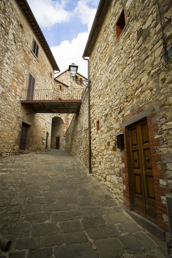 View of aged stone buildings line a narrow cobblestone street beneath a bridge in the old town San Gimignano Tuscany Italy.