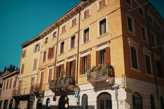 View of a historic yellow building with wooden shutters and balconies decorated with green plants under a clear blue sky in Verona Veneto Italy.