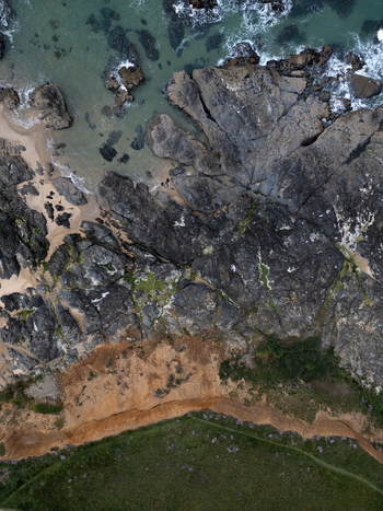Aerial view of the rugged coastline at Godrevy Beach featuring dark jagged rocks turquoise water and a cliffside path in Gwithian England United Kingdom. Aerial view of the rugged coastline at Godrevy Beach featuring dark jagged rocks turquoise water and a cliffside path in Gwithian England United Kingdom.