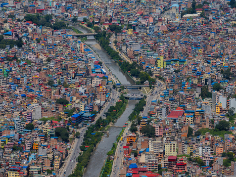 Aerial view of a dense urban cityscape featuring a river flowing through the center multiple bridges and closely packed multi story buildings under a clear sky in Nepal.