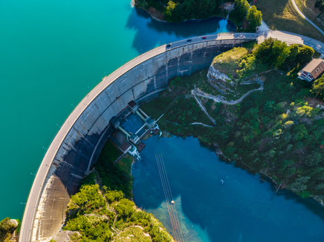 Aerial view of Barrage de Rossens dam with turquoise water surrounding lush green forests and a road running along the top in Pont la Ville Fribourg Switzerland.