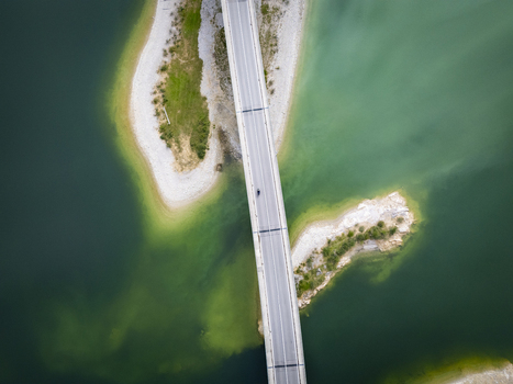 Aerial view of a lone figure traversing a concrete bridge embraced by the teal waters of Sylvensteinspeicher Lake Bavaria Germany. Aerial view of a lone figure traversing a concrete bridge embraced by the teal waters of Sylvensteinspeicher Lake Bavaria Germany.