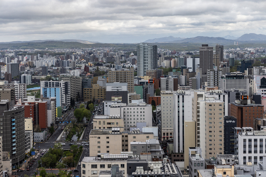 Aerial view of the dense urban cityscape of Sapporo featuring high rise buildings residential blocks and busy streets under a cloudy sky in Sapporo Hokkaido Japan. Aerial view of the dense urban cityscape of Sapporo featuring high rise buildings residential blocks and busy streets under a cloudy sky in Sapporo Hokkaido Japan.