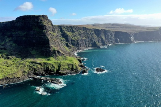 Aerial view of Neist Point featuring dramatic cliffs lush green slopes and deep blue sea in Isle of Skye Scotland United Kingdom. Aerial view of Neist Point featuring dramatic cliffs lush green slopes and deep blue sea in Isle of Skye Scotland United Kingdom.