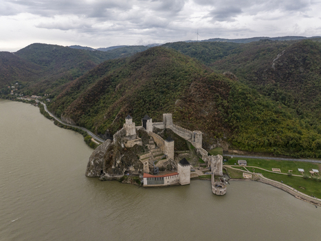 Aerial view of Golubac Fortress situated on the rocky banks of the Danube River surrounded by lush green hills under a cloudy sky in Golubac Branicevski okrug Serbia. Aerial view of Golubac Fortress situated on the rocky banks of the Danube River surrounded by lush green hills under a cloudy sky in Golubac Branicevski okrug Serbia.