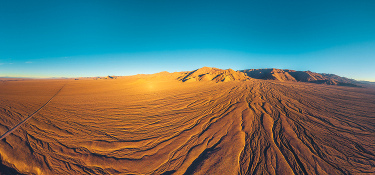 Aerial view of the vast arid Atacama Desert landscape with textured sand dunes distant mountains and a long straight road under a clear blue sky in San Pedro de Atacama Antofagasta Chile. Aerial view of the vast arid Atacama Desert landscape with textured sand dunes distant mountains and a long straight road under a clear blue sky in San Pedro de Atacama Antofagasta Chile.
