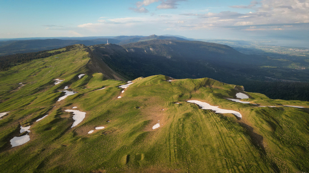 Aerial view of Le Colomby de Gex mountain ridge with green grassy slopes and melting snow patches in the Jura Mountains Echenevex Auvergne Rhone Alpes France. Aerial view of Le Colomby de Gex mountain ridge with green grassy slopes and melting snow patches in the Jura Mountains Echenevex Auvergne Rhone Alpes France.