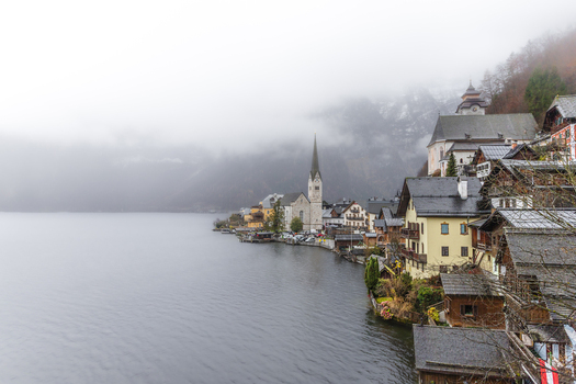 View of the historic village of Hallstatt with its iconic church spire and traditional alpine houses along the lake under a misty sky Hallstatt Upper Austria Austria. View of the historic village of Hallstatt with its iconic church spire and traditional alpine houses along the lake under a misty sky Hallstatt Upper Austria Austria.