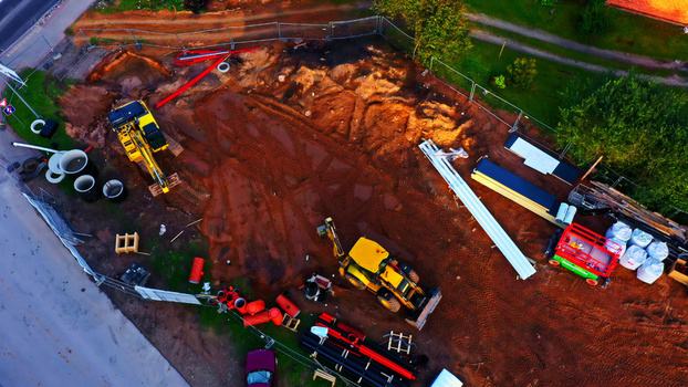 Aerial view of a construction site featuring yellow excavators piles of pipes and building materials on a dirt lot in Latvia. Aerial view of a construction site featuring yellow excavators piles of pipes and building materials on a dirt lot in Latvia.