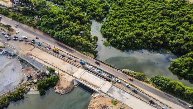 Aerial view of a road bridge crossing a river surrounded by dense mangrove forest with cars driving along the asphalt road in Ghana. Aerial view of a road bridge crossing a river surrounded by dense mangrove forest with cars driving along the asphalt road in Ghana.
