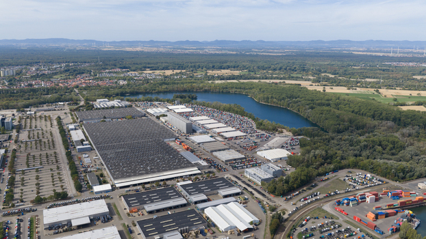 Worth am Rhein Germany 19 September 2026 Aerial view of the Mercedes Benz Werk Worth factory featuring large industrial buildings truck parking lots and a nearby lake with surrounding forest.