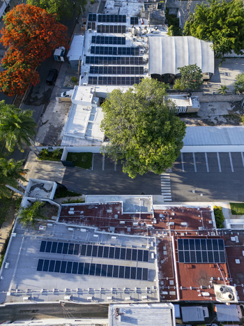 Aerial view of residential rooftops equipped with solar panels a large central tree and a parking lot in Merida Yucatan Mexico. Aerial view of residential rooftops equipped with solar panels a large central tree and a parking lot in Merida Yucatan Mexico.