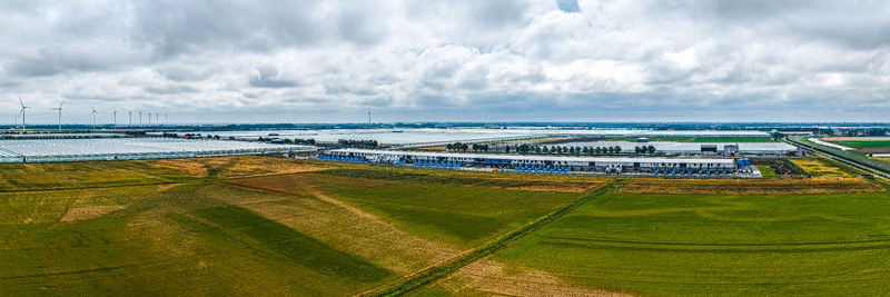 Aerial view of Agriport A7 greenhouse complex surrounded by agricultural fields and wind turbines under a cloudy sky in Middenmeer Noord Holland Netherlands. Aerial view of Agriport A7 greenhouse complex surrounded by agricultural fields and wind turbines under a cloudy sky in Middenmeer Noord Holland Netherlands.
